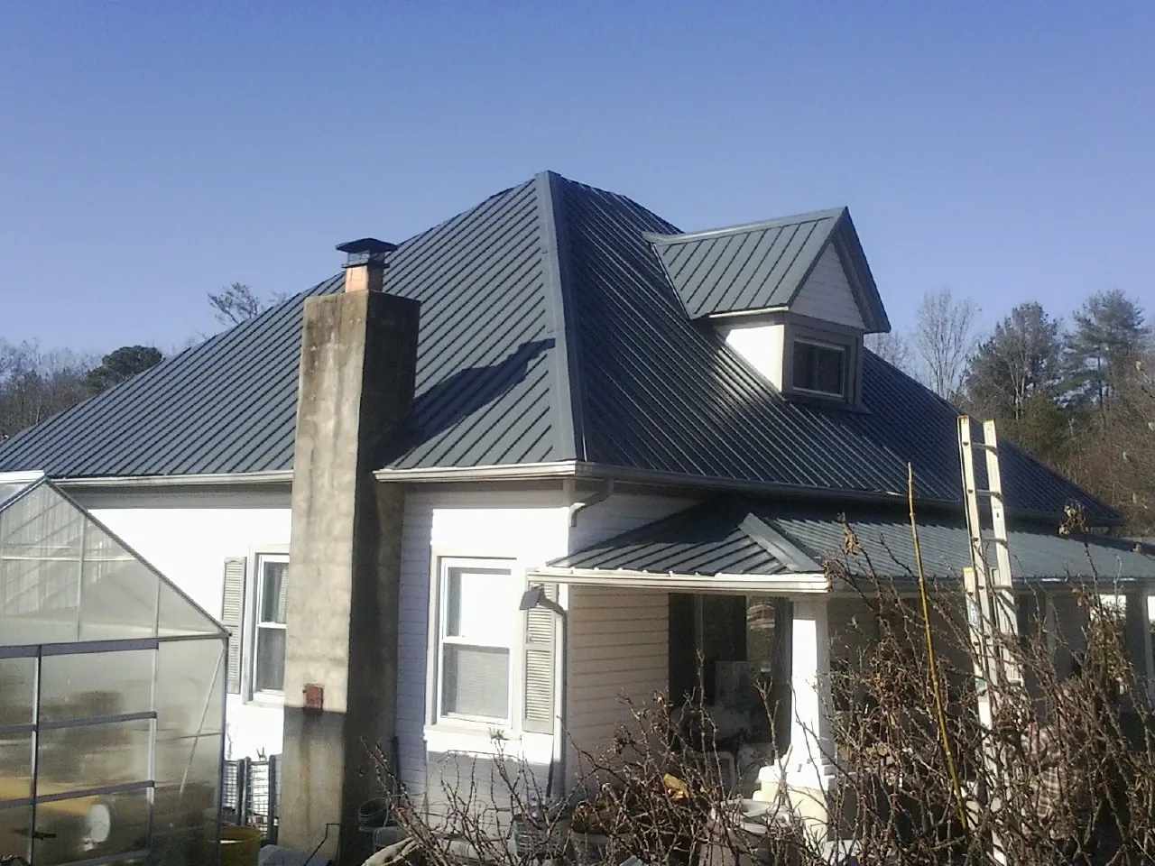 Dark blue standing seam metal roof on a white farmhouse with dormer — Slate & Tile Roof Repair by Roofing Brothers in Lake Worth