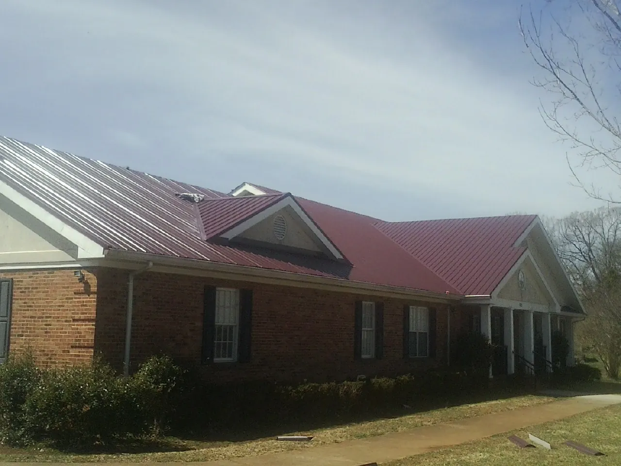 Red metal roof with gabled entries on a long brick building, from a Hail Damage Roof Repair job in Lake Worth
