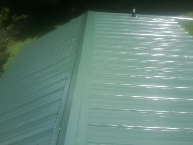 New green metal panels meeting at the ridge of a roof — Flat Roof Repair work by our crew in Lake Worth