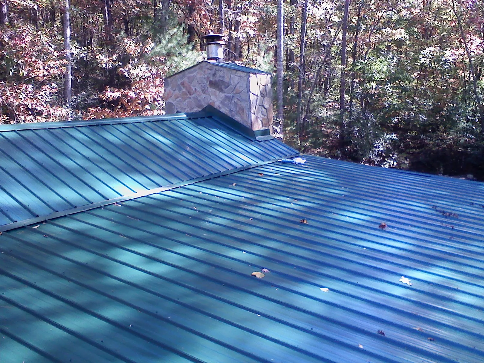 New green metal roof and stone chimney surrounded by autumn woods in Lake Worth