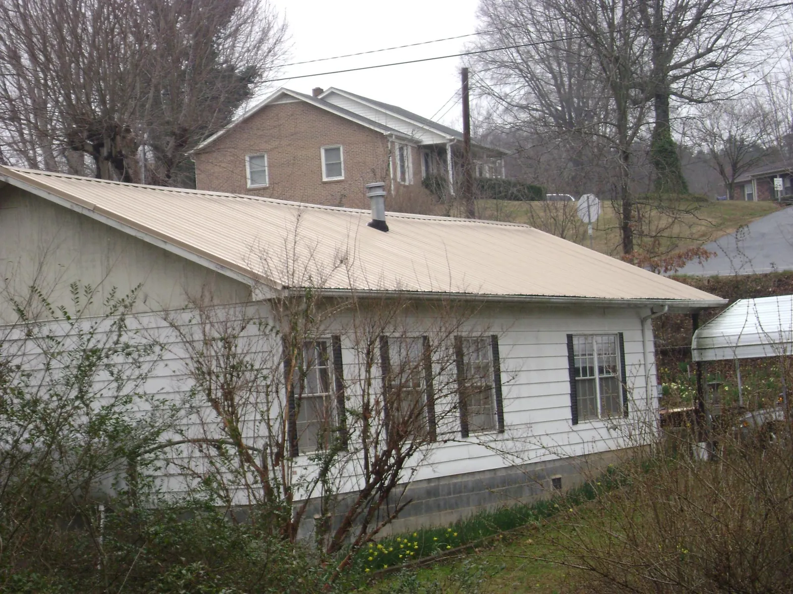 Tan metal roof on a white sided house set into a hillside — Commercial Roofing by Roofing Brothers in Lake Worth