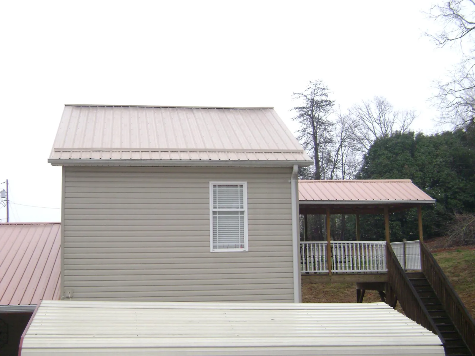 Tan metal roofs on a two story addition and attached porch, from a Roof Replacement job in Lake Worth